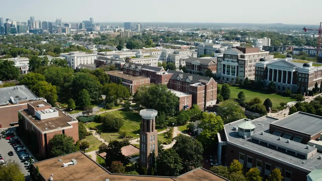 Aerial view of Belmont University’s campus just south of downtown Nashville, featuring red-brick academic buildings clustered among green lawns and trees, with the city skyline on the horizon.