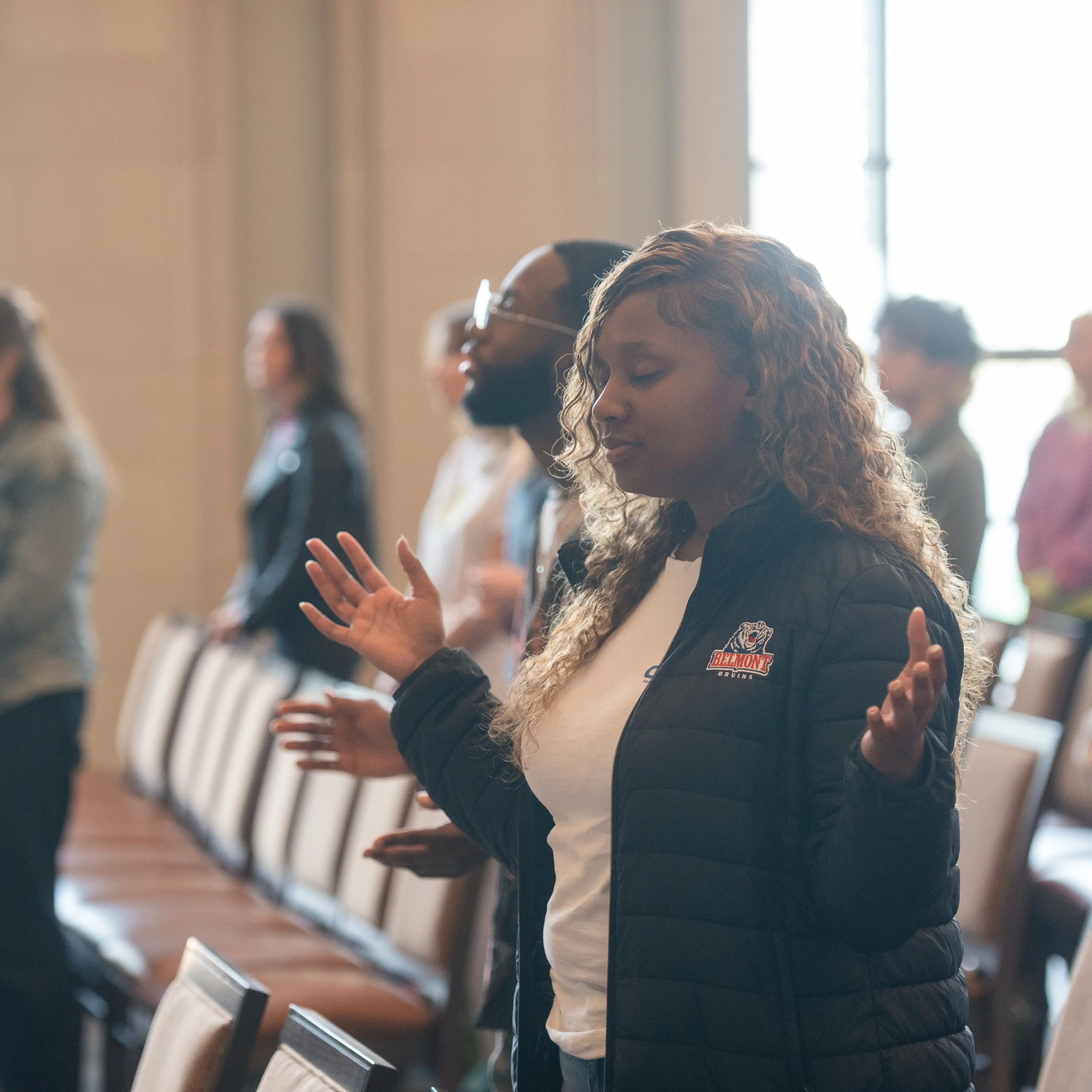 Student with eyes closed and hands raised in prayer during a campus worship service at Belmont.