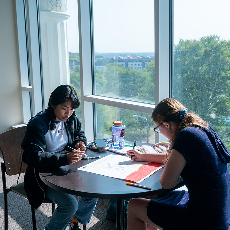 Two students working on a project together by a window