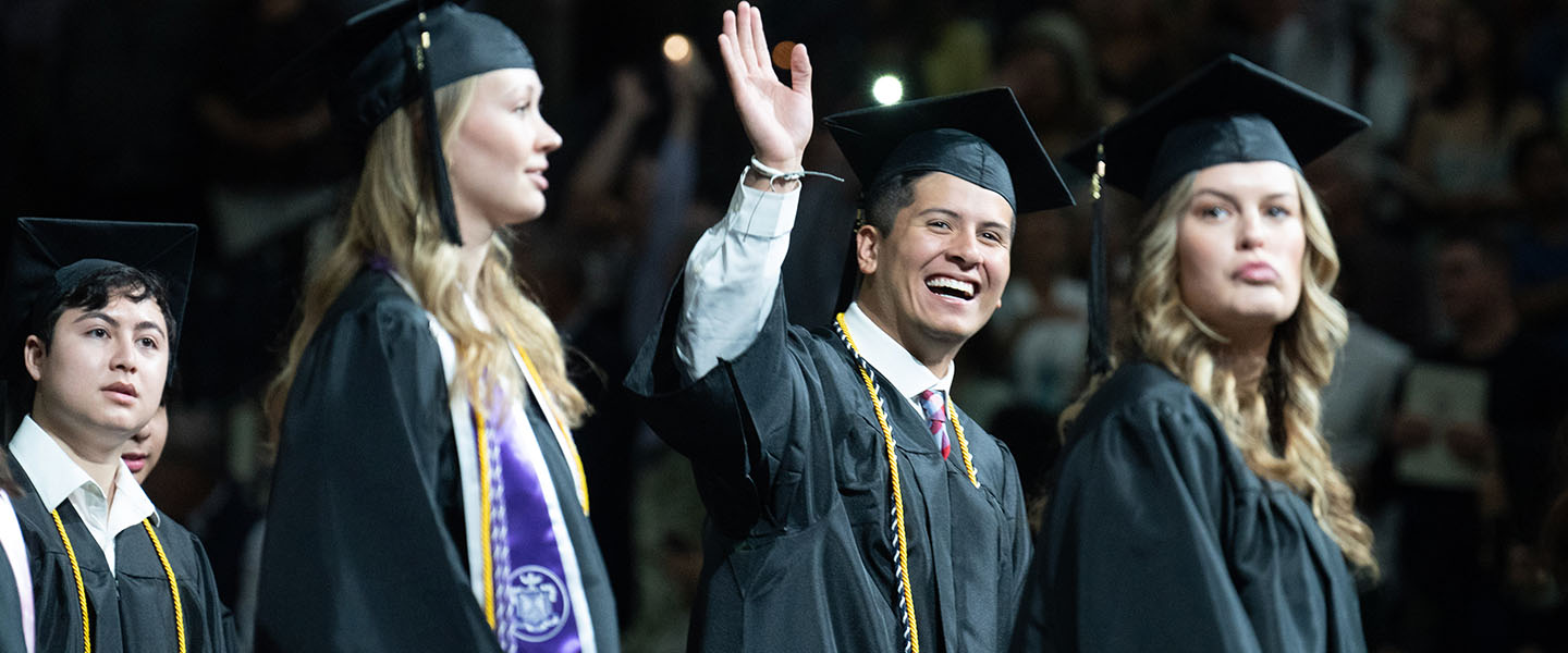 Belmont graduate smiles and waves at his family during graduation