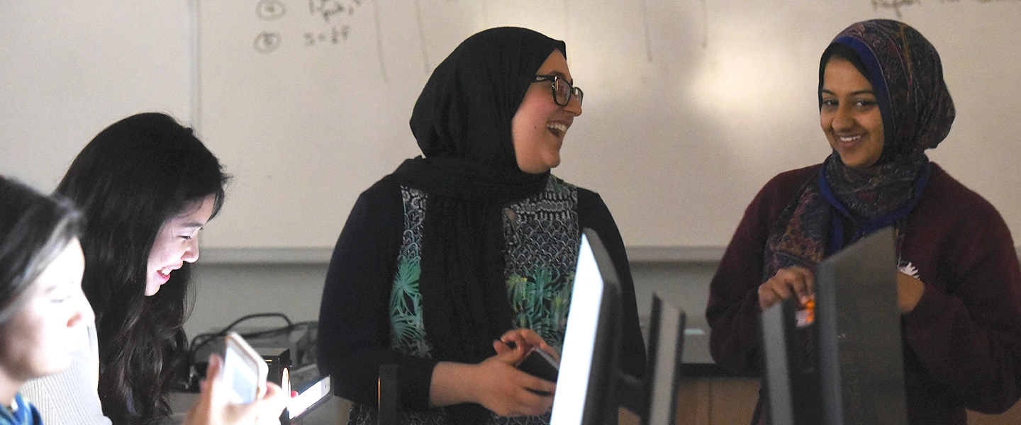 Two female students smile in a computer lab.