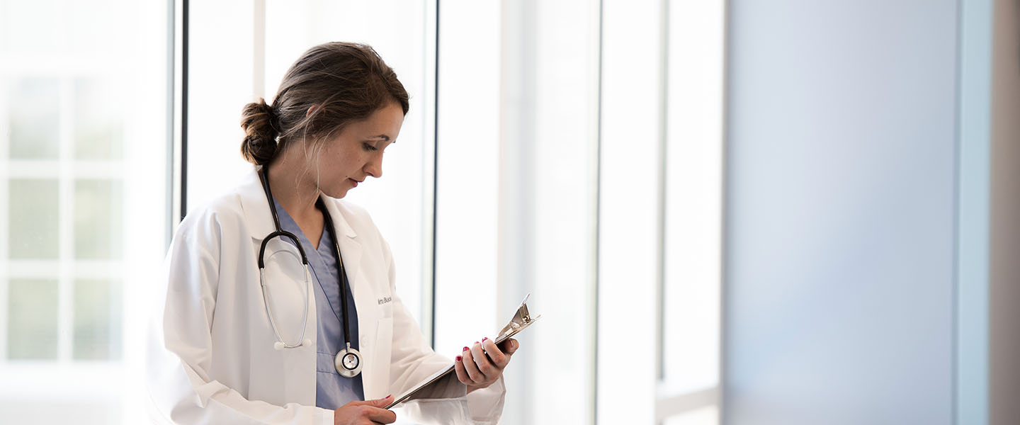 A nursing student looking at a chart next to a large window