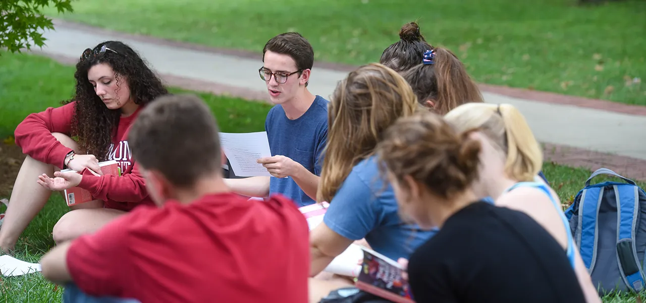 Male student sitting outside in class discussing something on a piece of paper