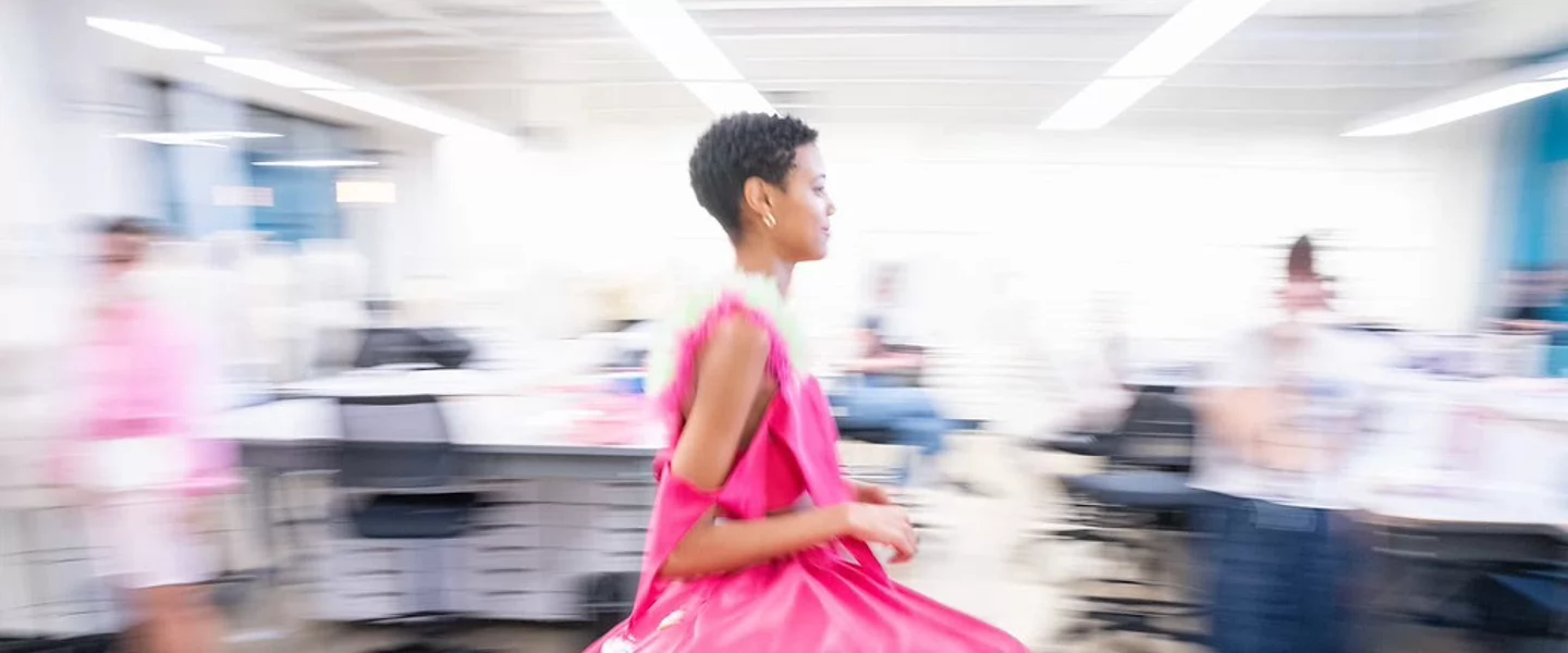 Fashion student models a garment while classmates observe in a design studio.