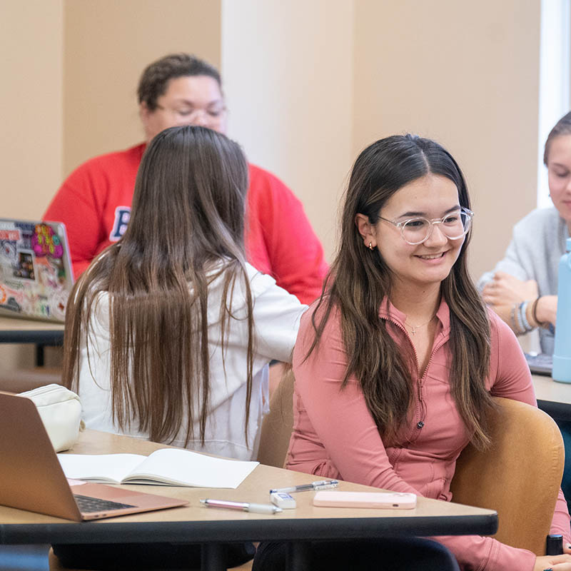 A student smiling while taking to other students during groups discussion in a classroom at a desk