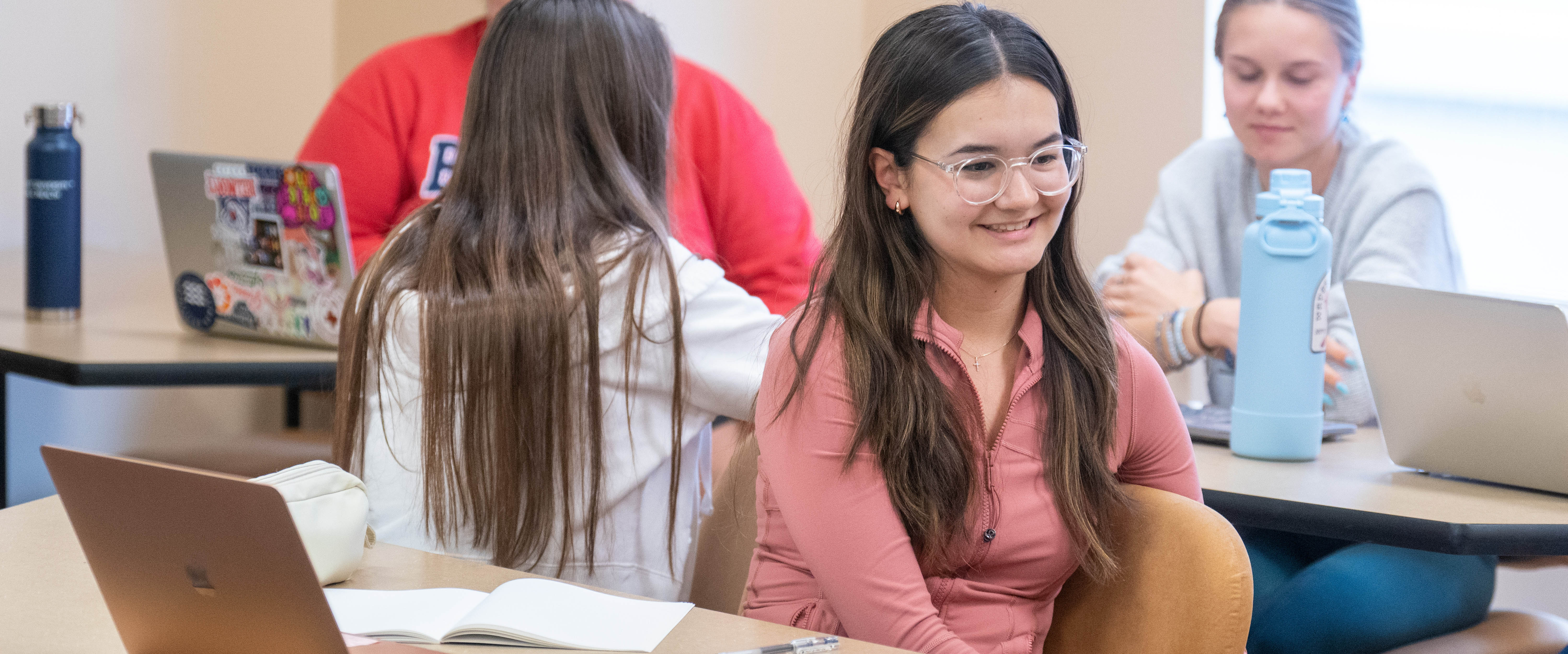 A student smiling while taking to other students during groups discussion in a classroom at a desk