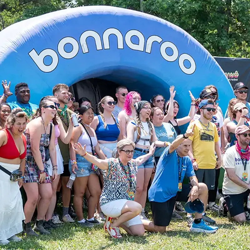 A group of people posing together in front of a large inflatable structure with the 'Bonnaroo' logo