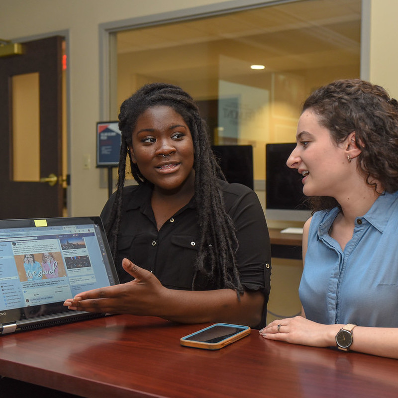 Two students explaining and talking about management work on a laptop