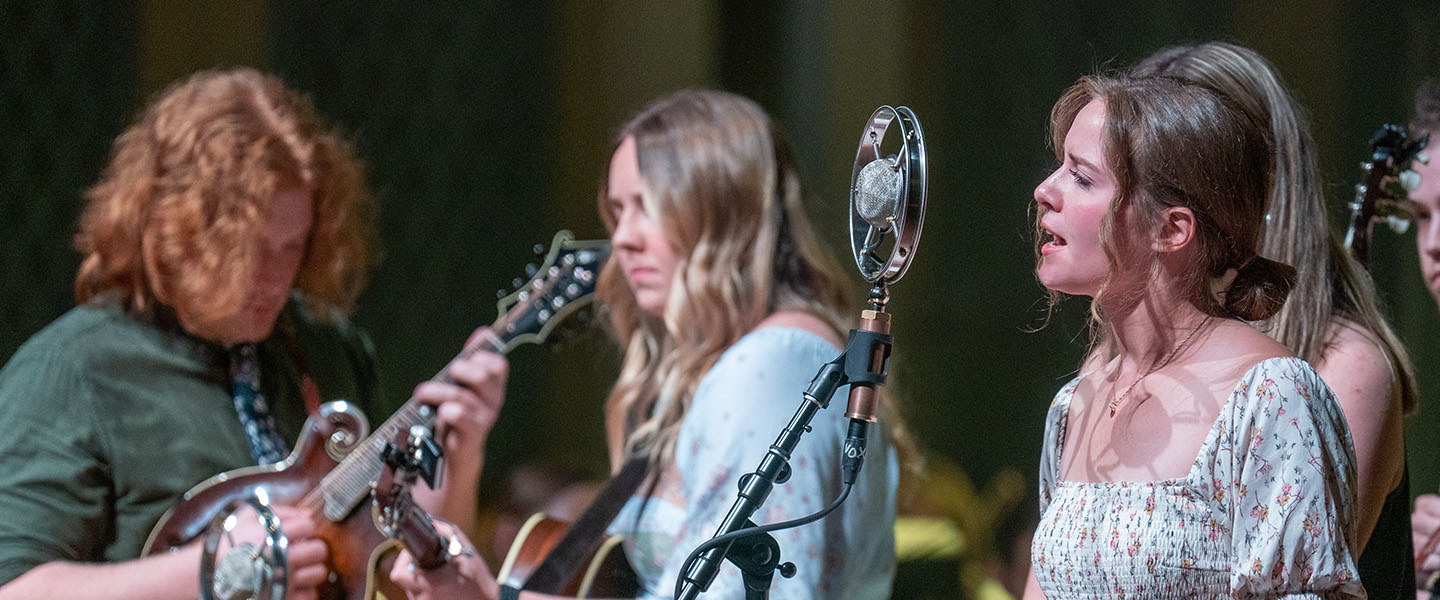 A trio of students appear to perform folk music on stage.