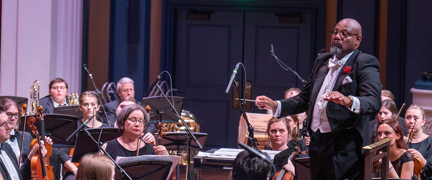 A conductor stands and leads an orchestra.