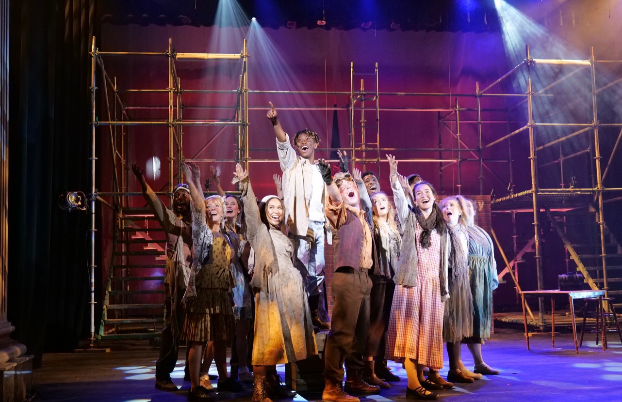 Student practice on stage during dress rehearsal for Urinetown