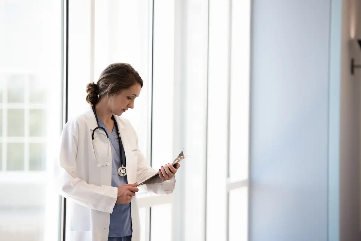 Nurse in scrubs stands in front of a window wall