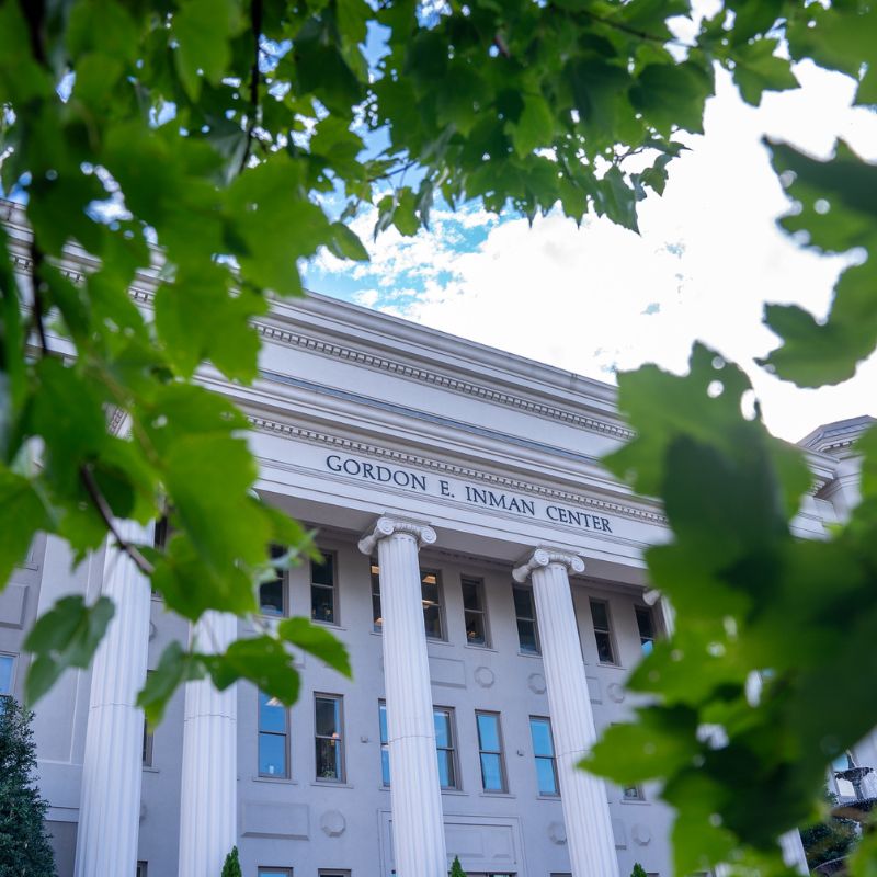 Exterior view of Belmont University’s Gordon E. Inman Center, framed by green leaves, showcasing the building’s white columns and classical architecture.