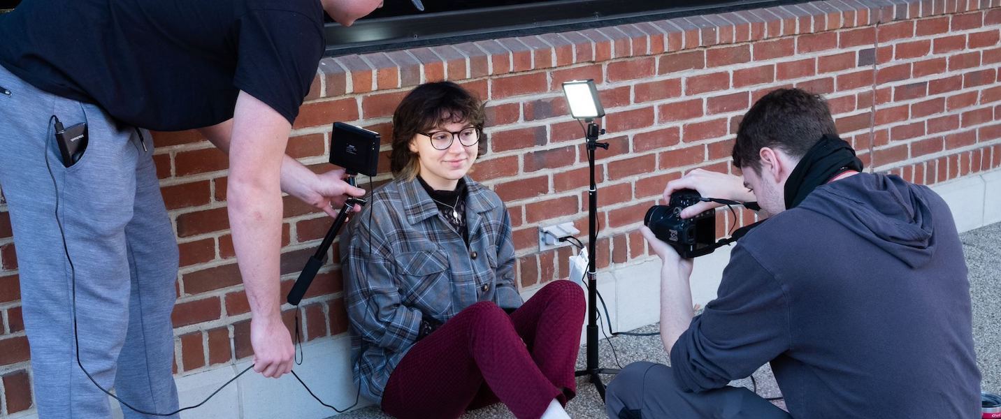 Three students taking photos outside of a brick building