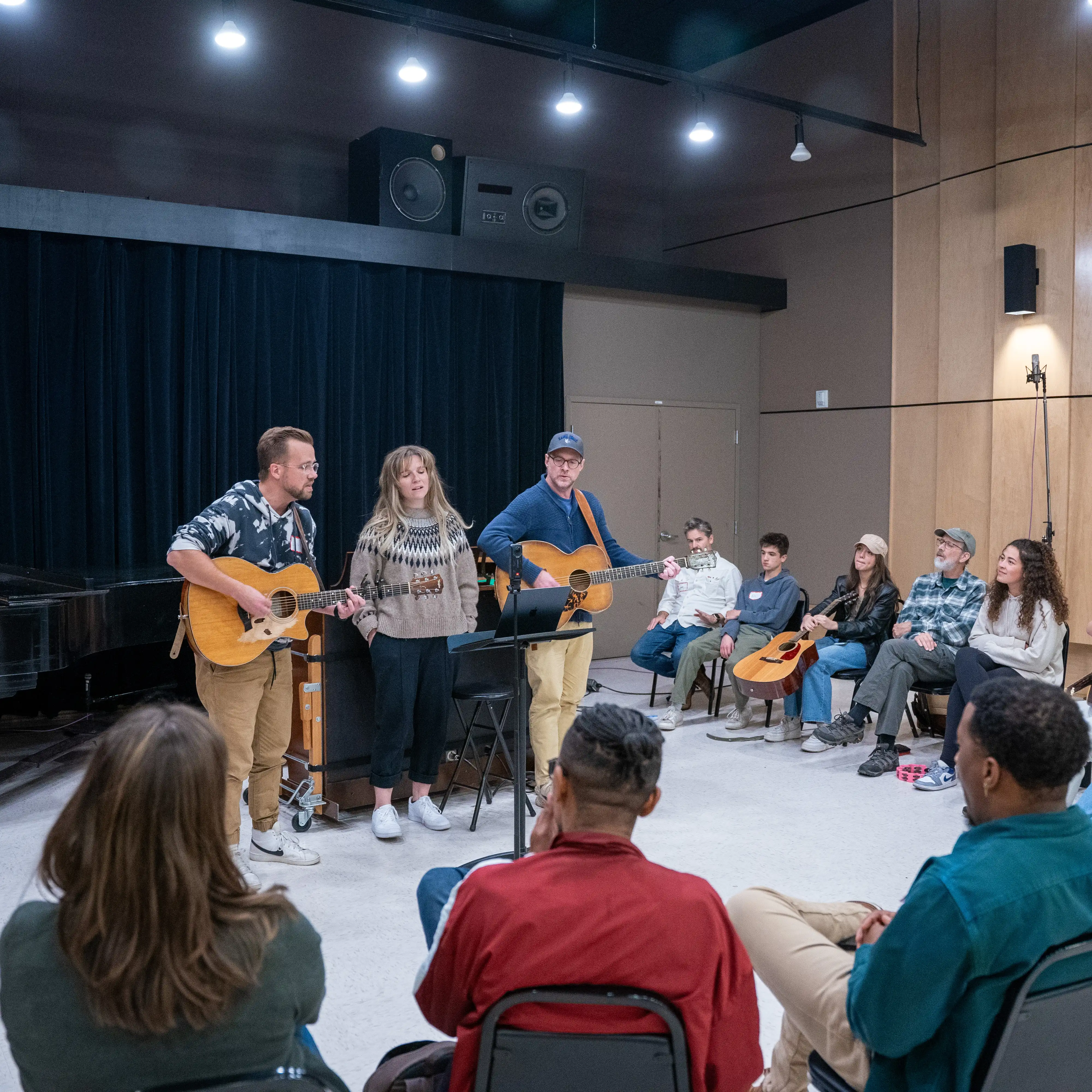 Students gather in a songwriting workshop as faculty and guest musicians perform original music, providing collaborative feedback and hands-on mentorship in a small-group setting.