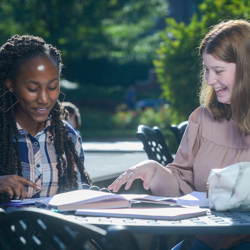 Two students chat at an outdoor table