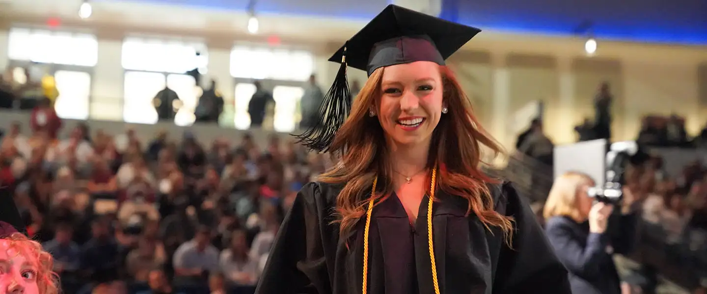 A female adult student smiling as she holds her diploma at graduation