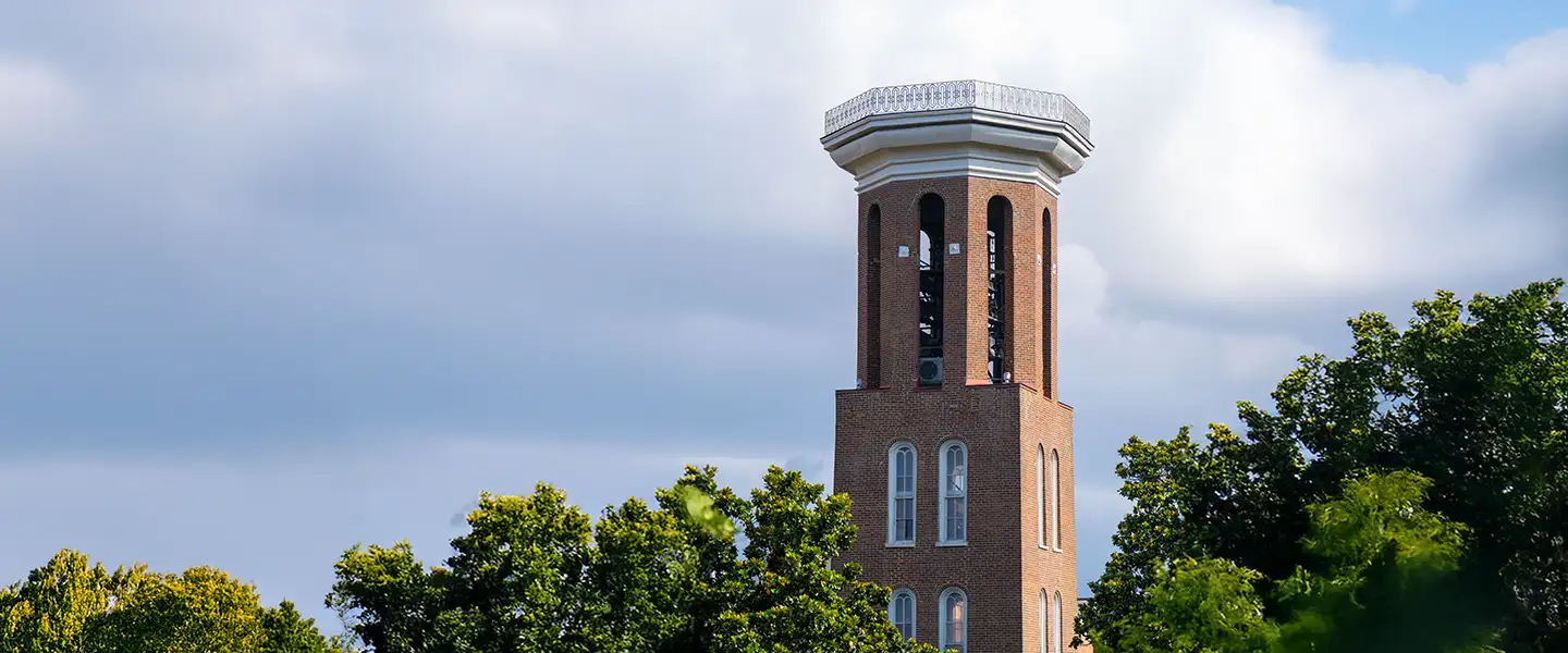 The Belmont University Bell Tower rises above green trees under a partly cloudy sky.