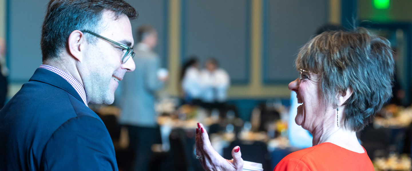 A man and a woman smile and laugh in conversation at a Belmont event.