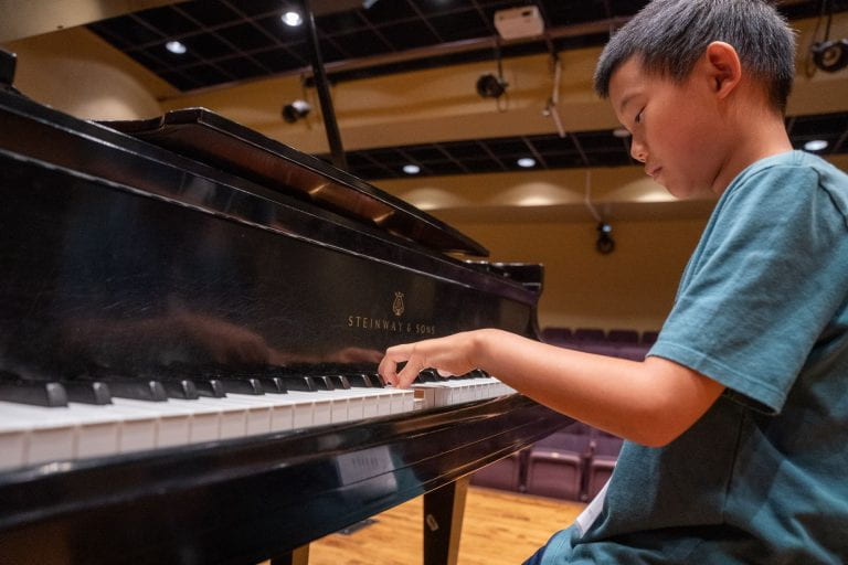 Close up photo of a boy playing piano in a large auditorium