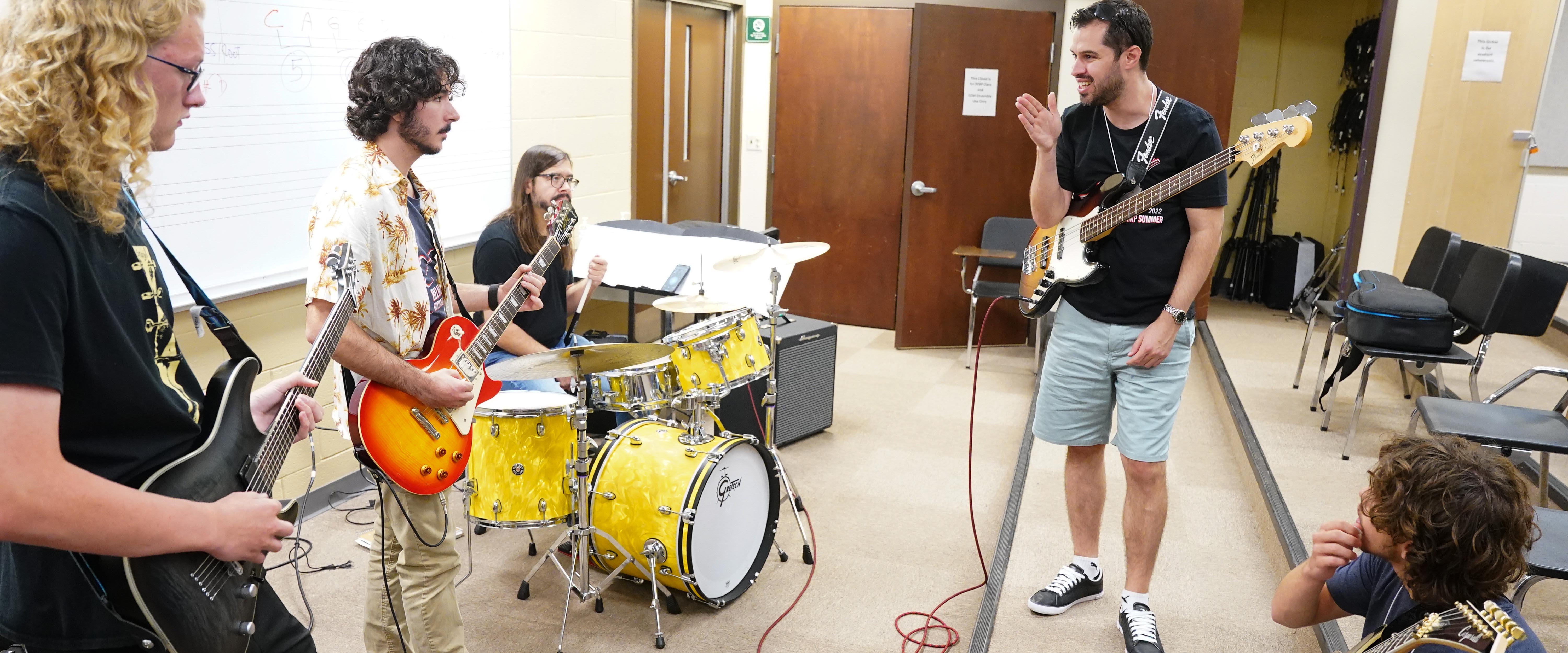 Students with guitars listen to teacher instruct the camp