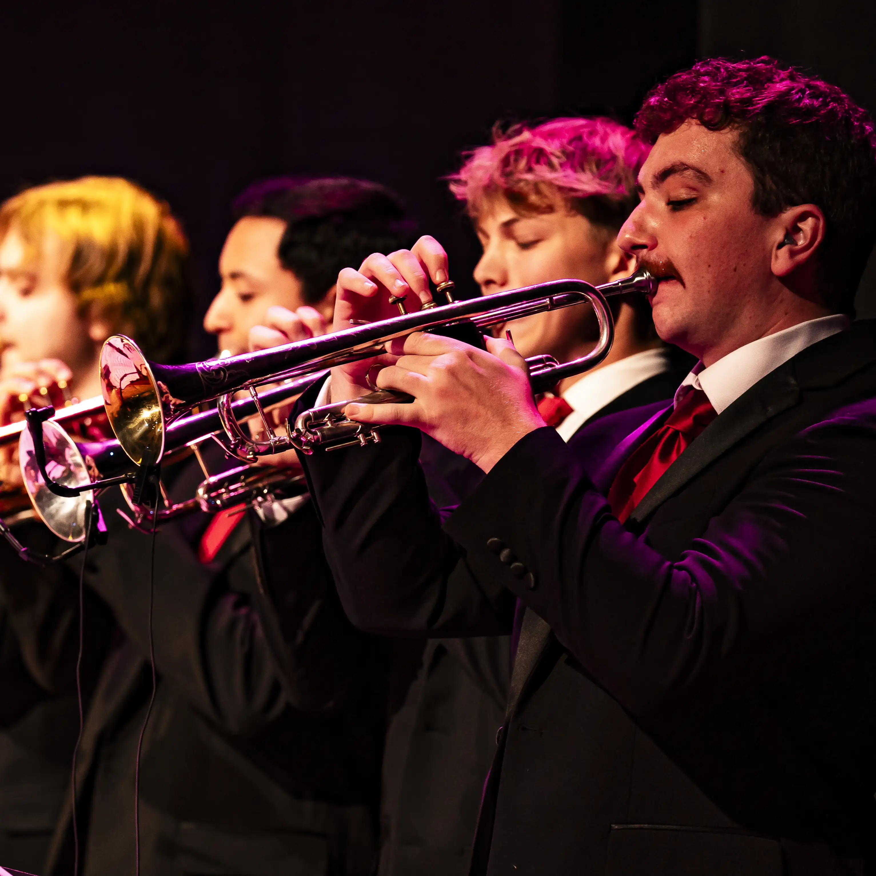 Belmont students play trumpets during a live ensemble performance on stage.