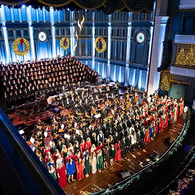 Belmont University choir and orchestra perform together onstage in a decorated concert hall during a holiday program.