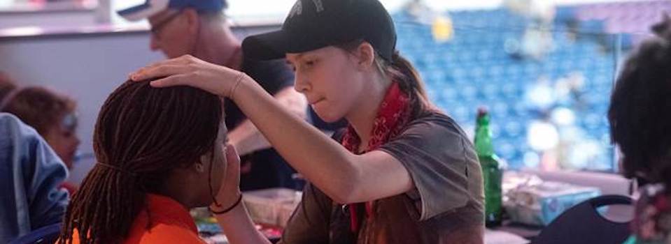 Photo of a student applying face paint to a child's face.