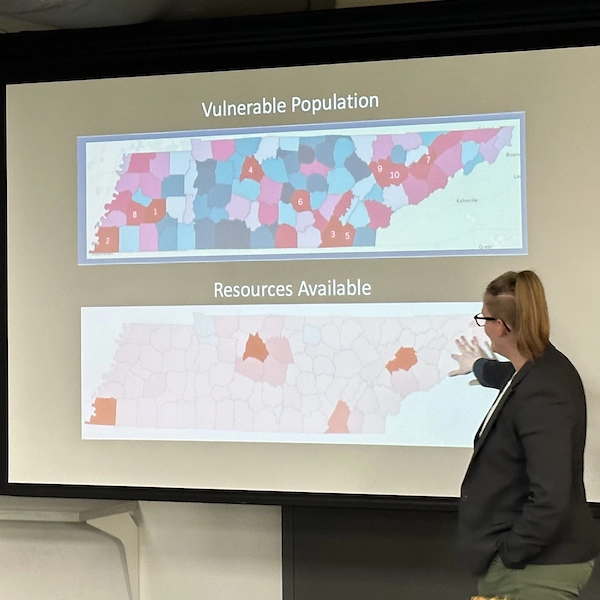 A woman presenting a data presentation about vulnerable populations, gesturing to a map