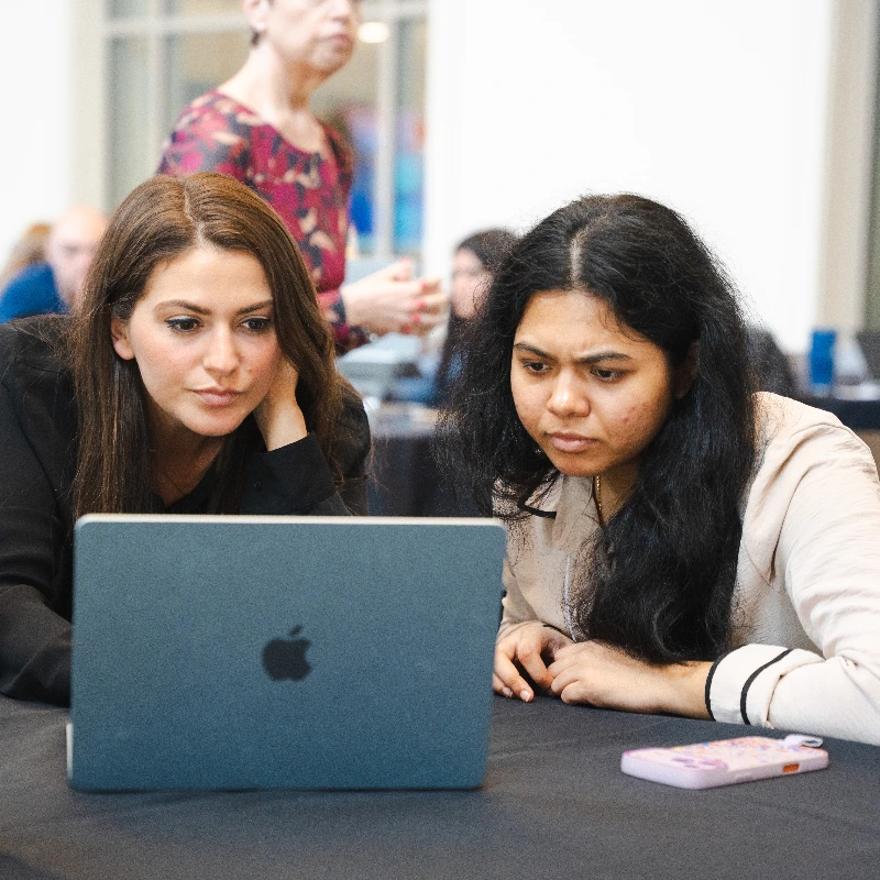Two women intently focused on a laptop screen, collaborating in a professional or educational setting.