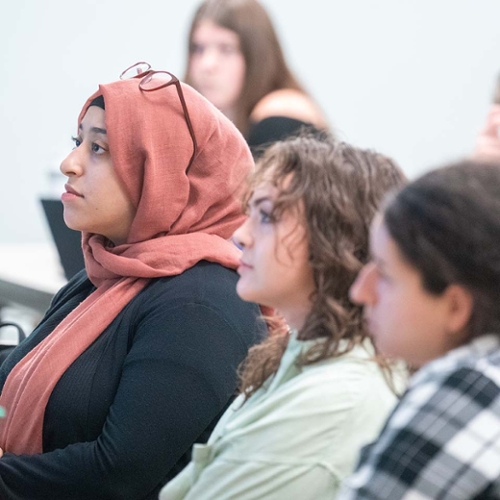 3 students listen to professor speak during class lecture