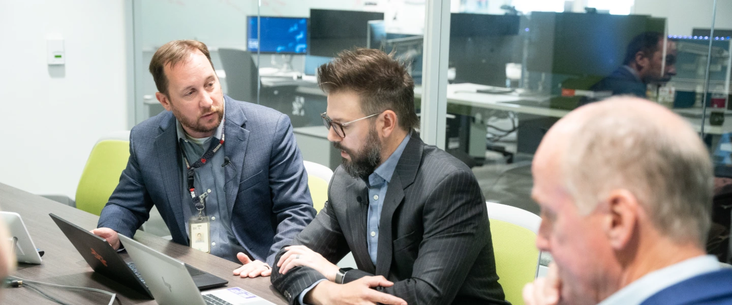 Business professionals discussing strategy in a modern office meeting room with laptops.