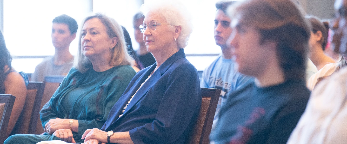 Audience of adults and students sitting and listening attentively at a conference or event.