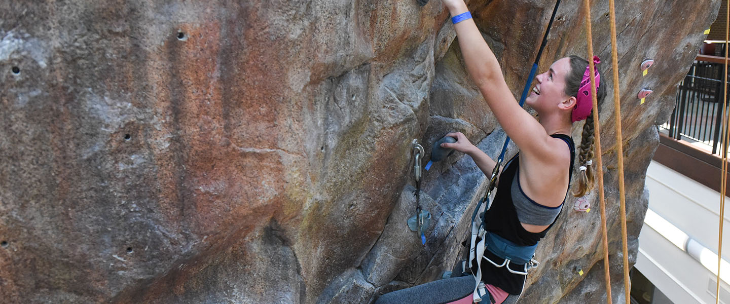 Student climbing the rock wall with a smile