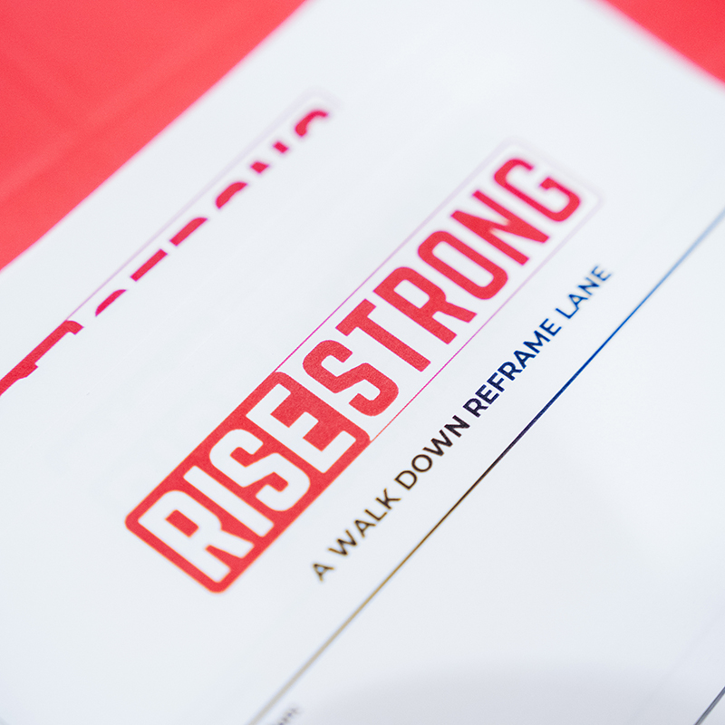 Close up of sheet of paper and with the text "RiseStrong: A Walk Down Reframe Lane"