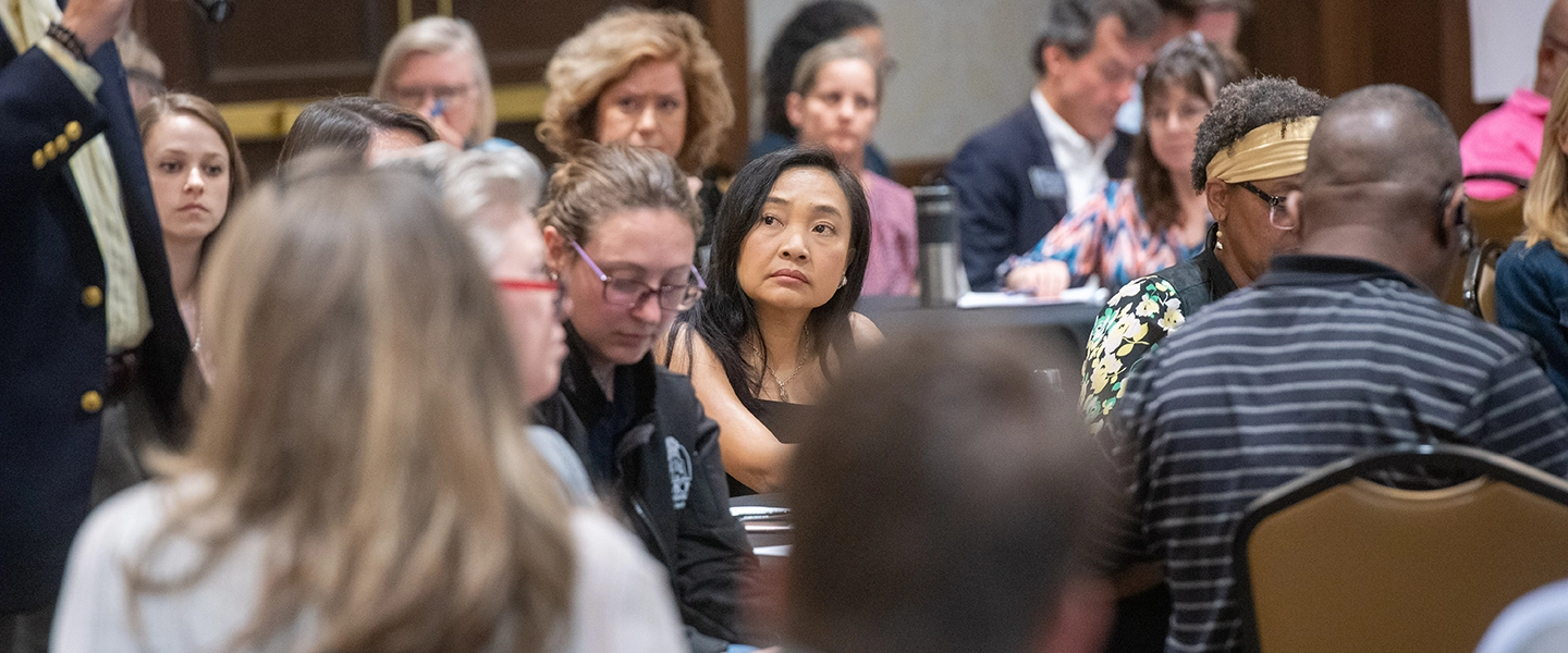 Group of people seated at tables in a conference setting, listening intently during a discussion or presentation.