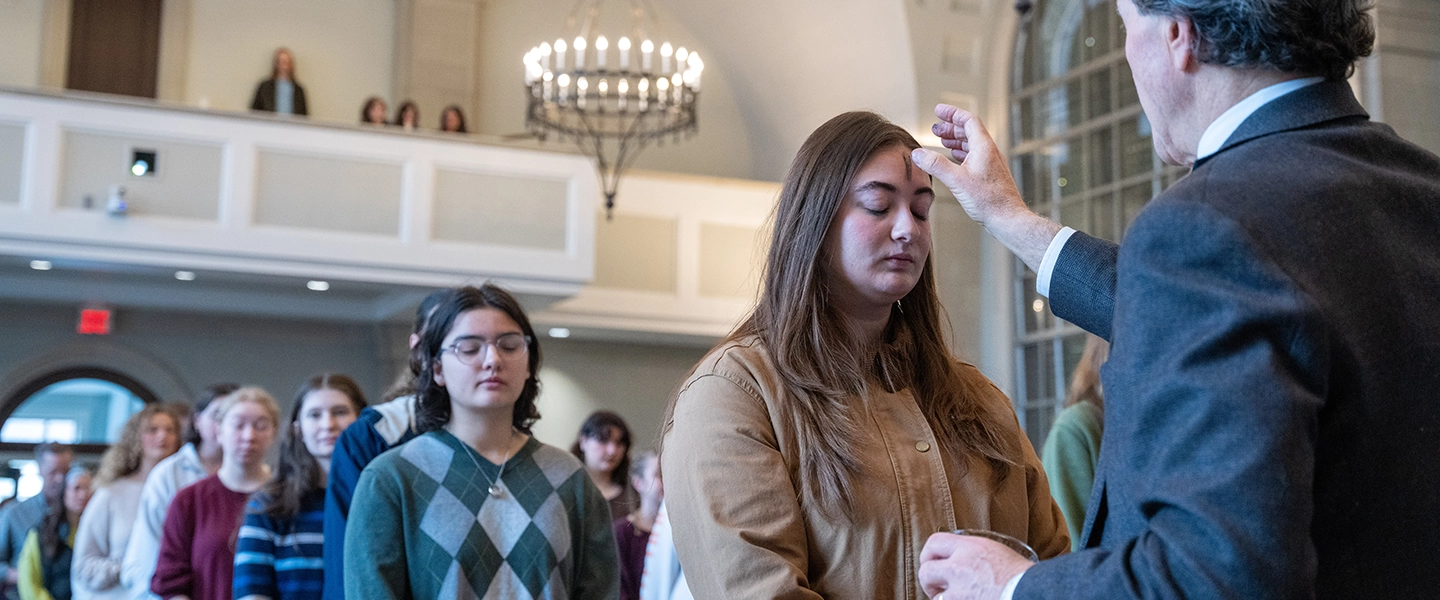 Students in a chapel service line, one receiving an ash cross on their forehead during a religious observance.