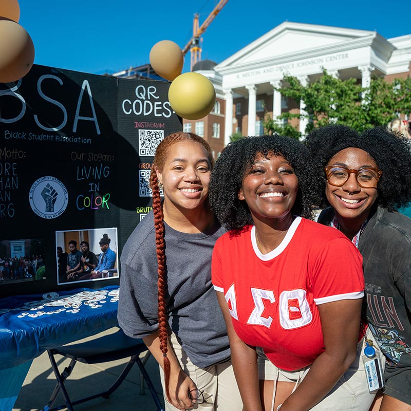 3 students smiling for the camera in front of a BSA poster board at the student clubs fair