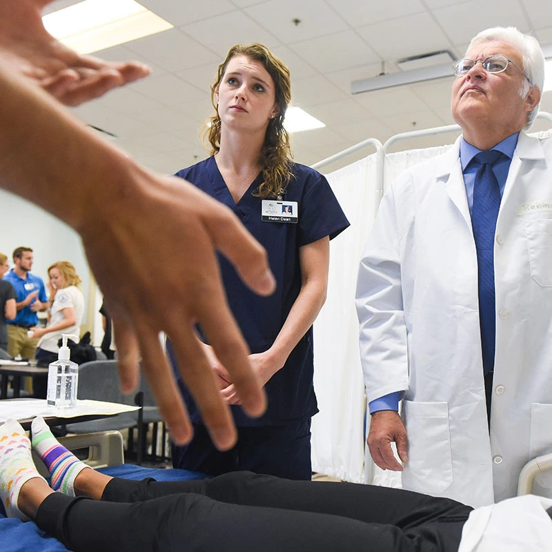 A student and a doctor talk with an actor during a live simulation.