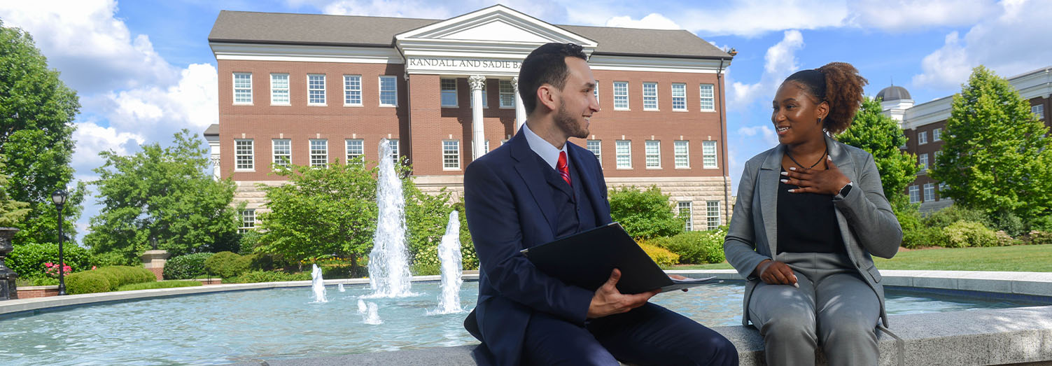 Two law students sitting on the Freedom Plaza Fountain with the Baskin Center in the background