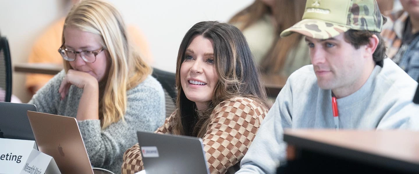 Students at tables in class room listening to class lecture with their laptops open