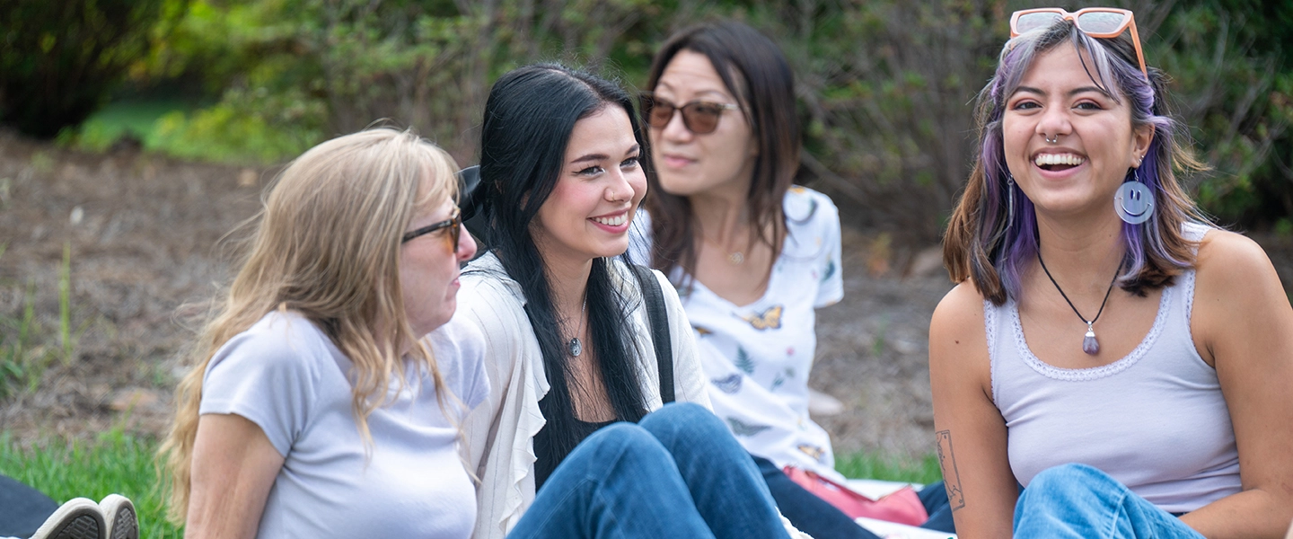 Students laughing and smiling while sitting on lawn during parents weekend