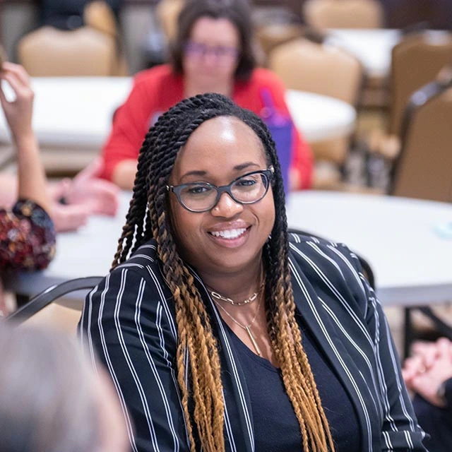 Woman sitting down and smiling at the people around her during group table discussion at talk.