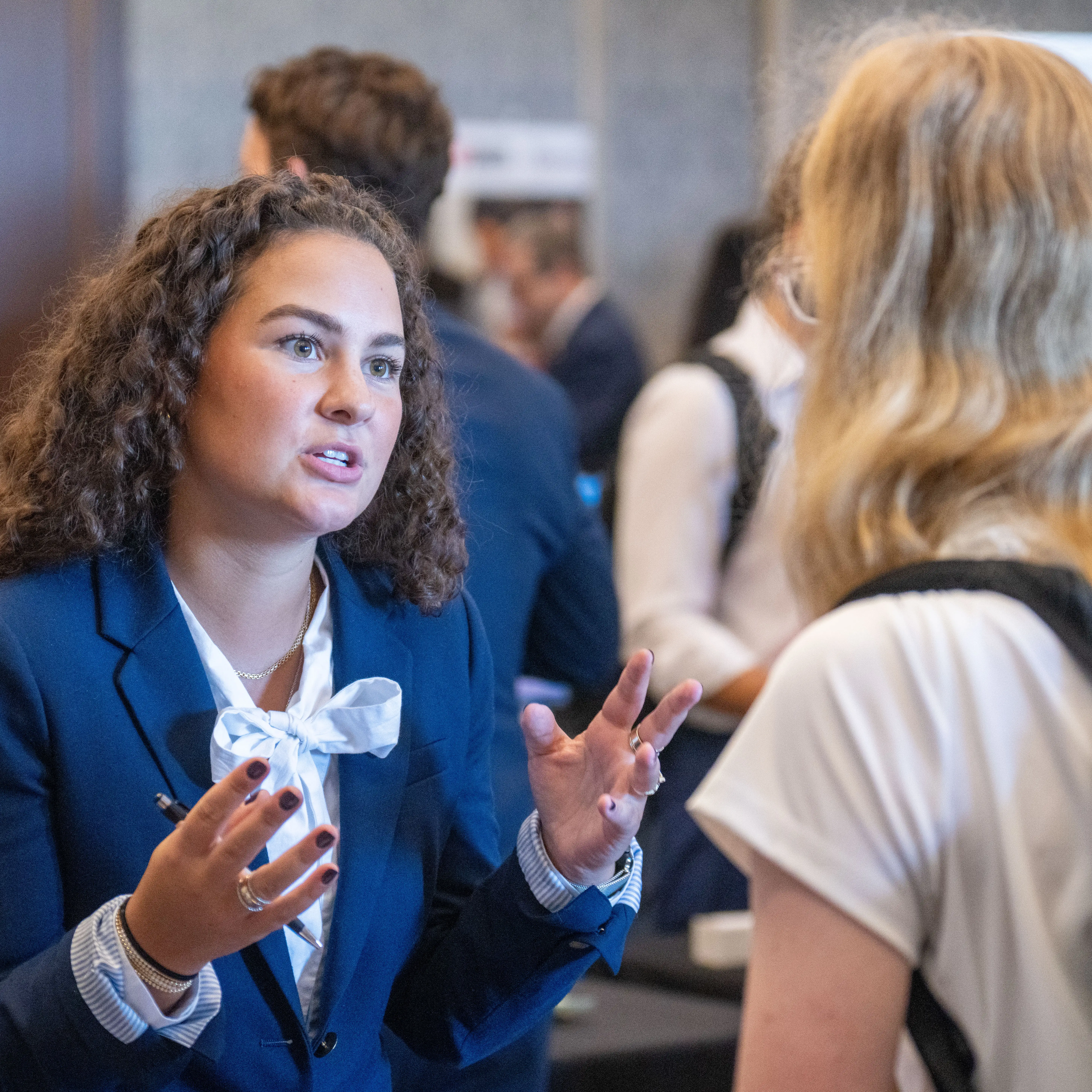 Student in professional attire speaking with another attendee during a networking event.
