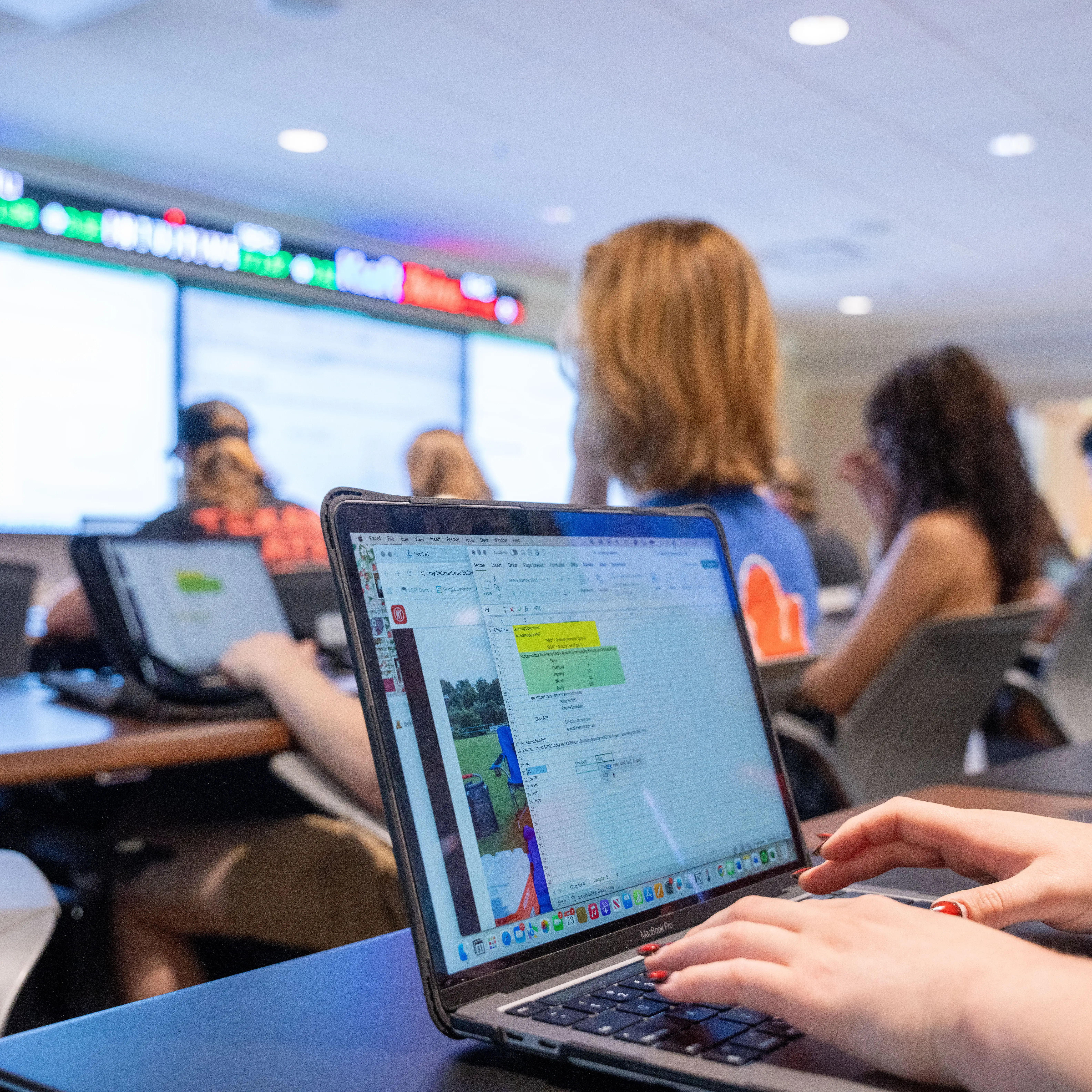 Student using a laptop during a class session with financial data displayed on screen.