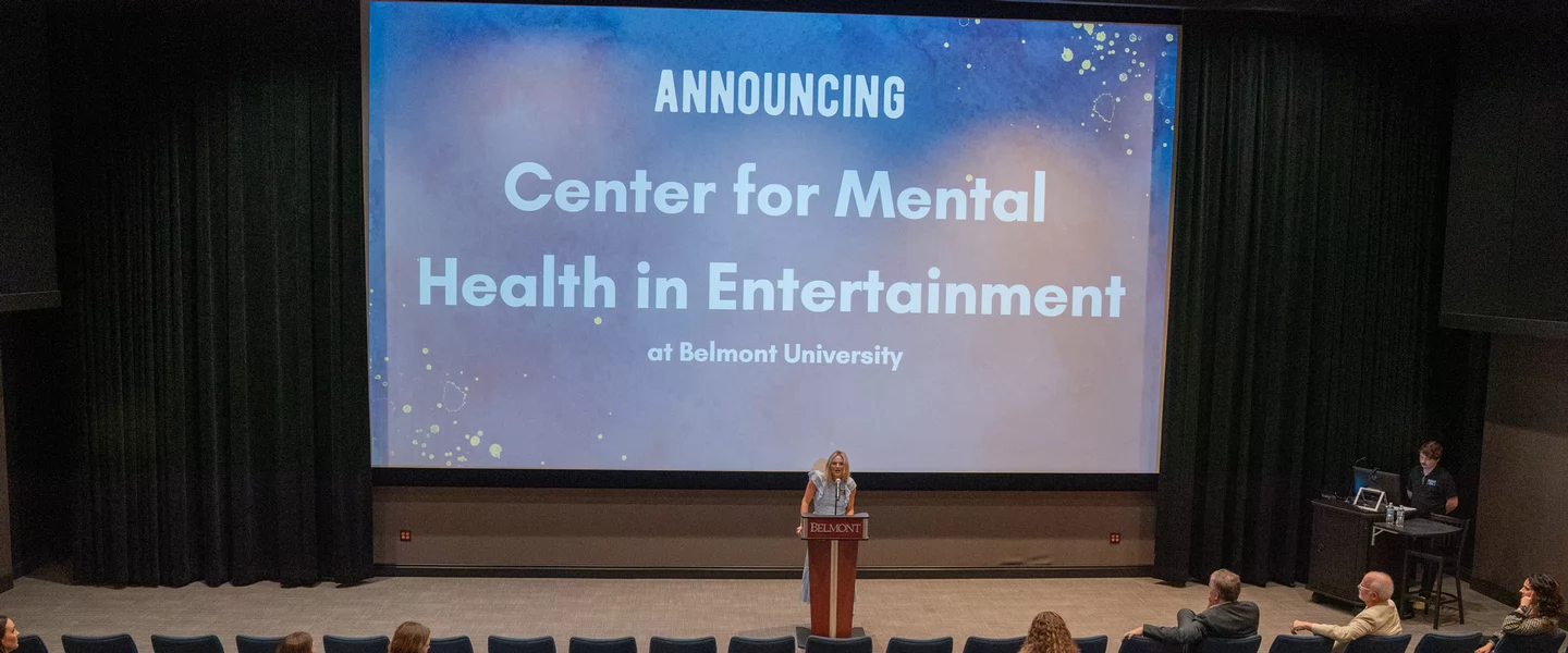 Brittany Schaffer stands at a podium in an auditorium as a screen announces the launch of the Center for Mental Health in Entertainment at Belmont University.