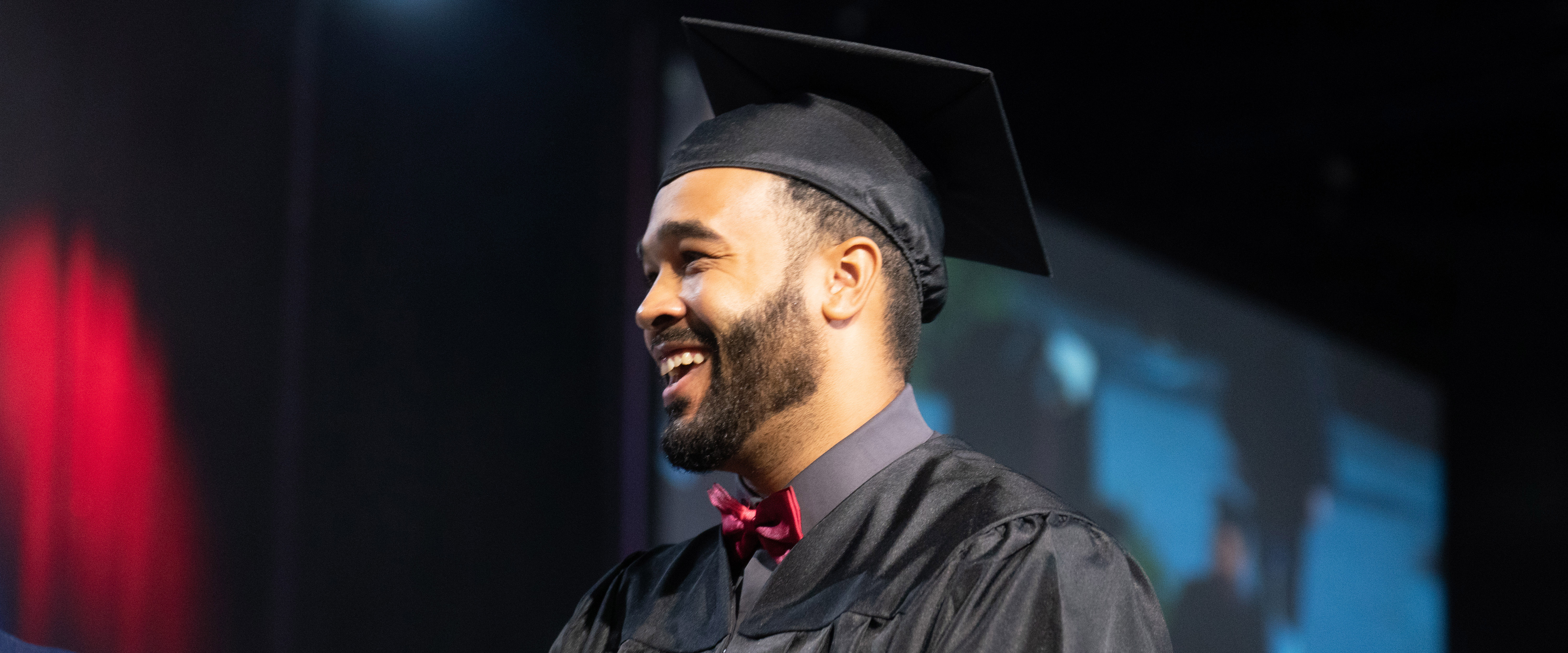 Student in cap and gown on stage receiving their diploma 