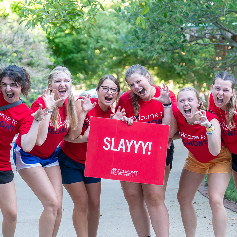 Orientation leaders growling like a bear and holding a sign that says Slay! during move in