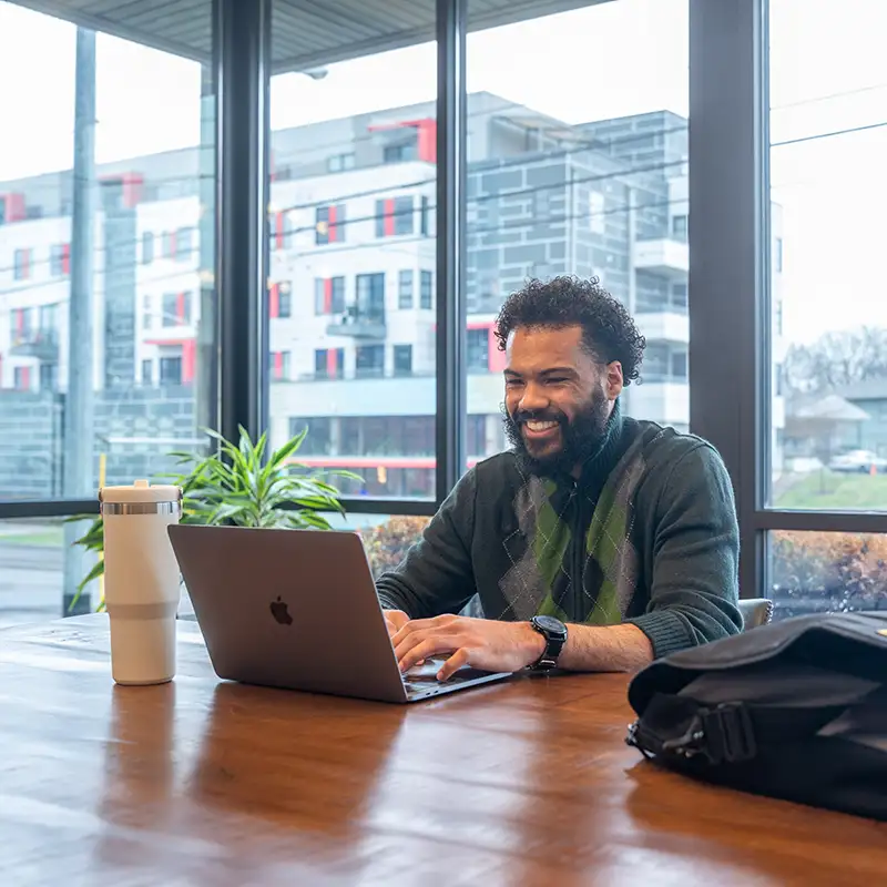 Man smiling while working on his laptop in a coffee shop