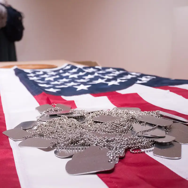 Close up of an American flag with a pile of blank dog tags on top of it during the art instillation for CreatiVets | Healing Through Art